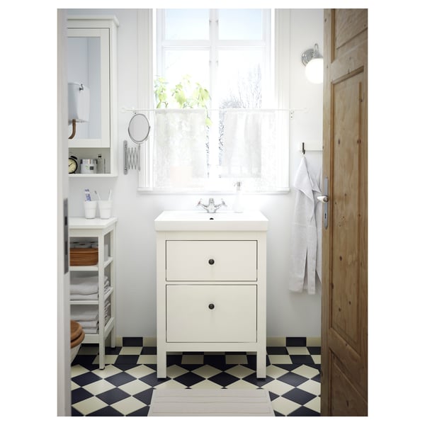 Small white bathroom sink vanity with two drawers, black and white chequered floor. Bright and minimalist design, wood door to the side.