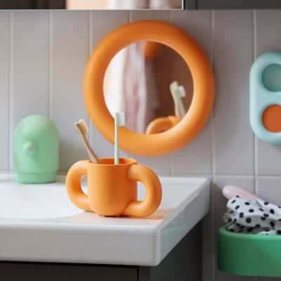 Colourful kids bathroom setup: round orange toothbrush holder, mirror, & storage, perfect for small hands.