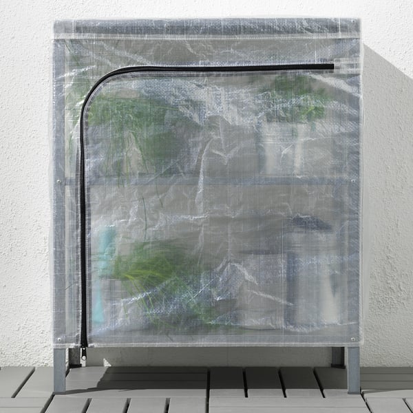 A transparent plastic cover on a shelving unit, likely used as a mini greenhouse. It protects contents from dust and allows air circulation.