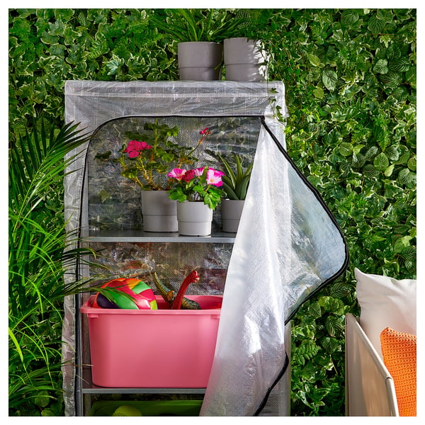 Small greenhouse with pink tools, pink flowers, and grey pots on shelves. White cover and mesh sides.