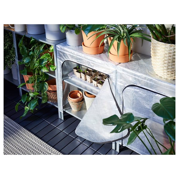 Small greenhouse with various potted plants on grey shelves. Cover has mesh sides for air circulation.