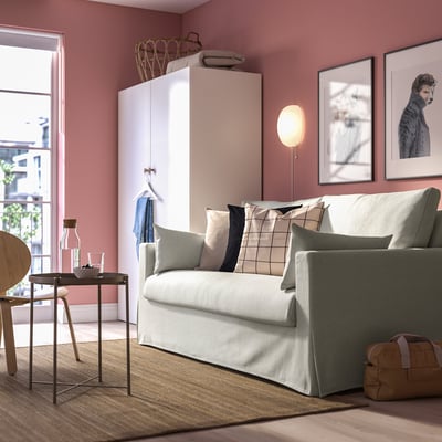 Modern living room: grey sofa, green cushions, pink walls, dog art, floor lamp, vases, rug, bag, window.