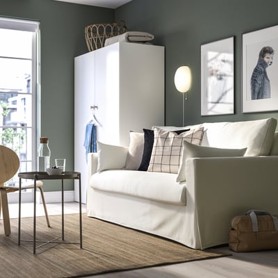Modern living room with white HYLTARP sofa-bed, pillows, side table, rug, floor lamp, and artwork.