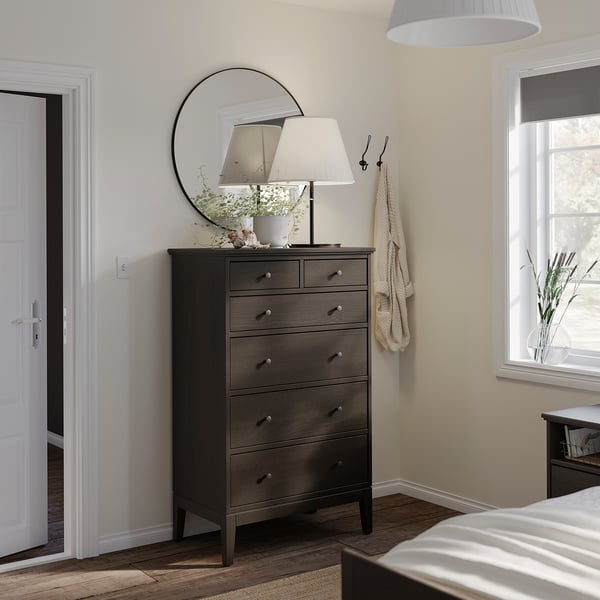 Modern bedroom with dark wood tall dresser, white lamp, mirror, window, and doorway.