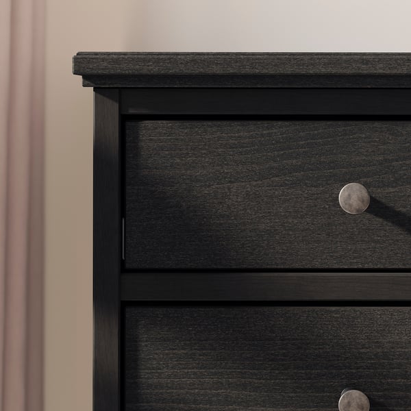 Black wooden chest of drawers with rounded knobs against a pink wall.