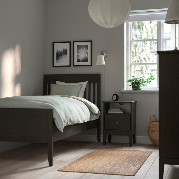 Minimalist modern bedroom: IDANÄS dark grey bed, minimalist bedside table, pendant light, grey rug, and basket with plant.