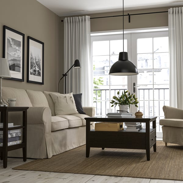 Modern living room with beige sofa, armchair, rectangular IDANÄS coffee table, and large window with white curtains.