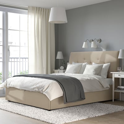 Beige IDANÄS ottoman bed, sloped headboard, white bedding, grey throw, bedside table, lamps.