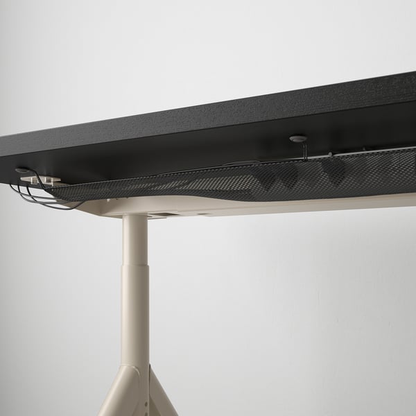 Black desk with cable management net underneath, supported by a beige adjustable leg.