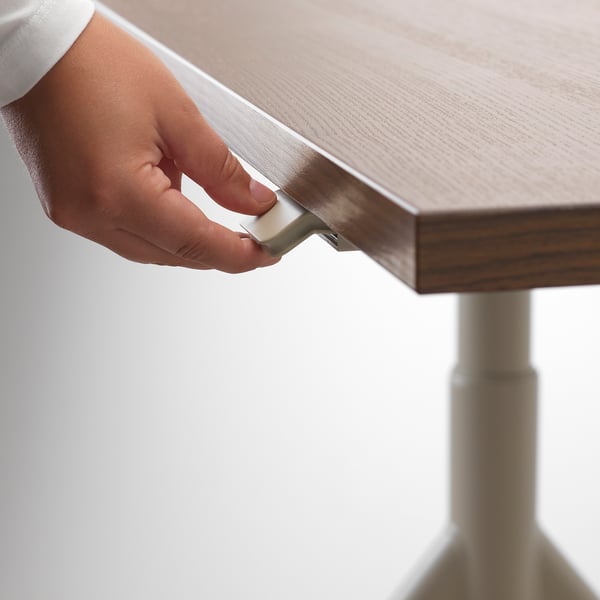 A hand adjusts a height-adjustable desks handle, demonstrating the mechanism for switching between sitting and standing positions.