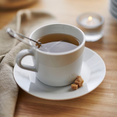 A white ceramic cup on a saucer with a spoon and sugar cubes, likely part of the IKEA 365+ series, designed for durability and everyday use.