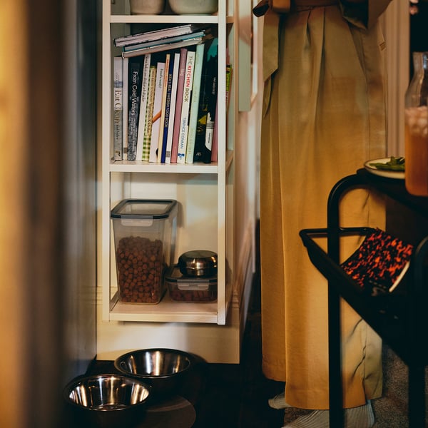 Shelf with clear pet food container, bowls, and books. Efficient storage, easy access.
