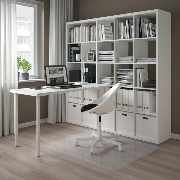 Modern home office with white INLÄGG desk, chair, kallax shelf with books, laptop, and lamp. Compact but functional setup.