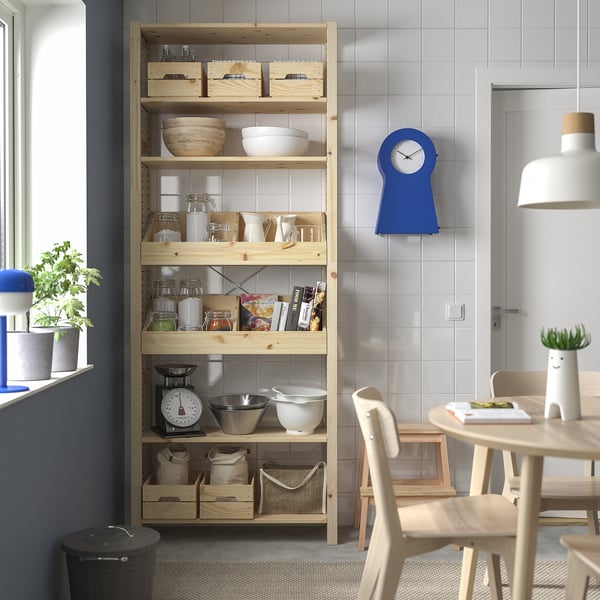 Wooden IVAR shelves with pine finish hold kitchen items, a blue clock, and a white lamp. Space-efficient under a high window.
