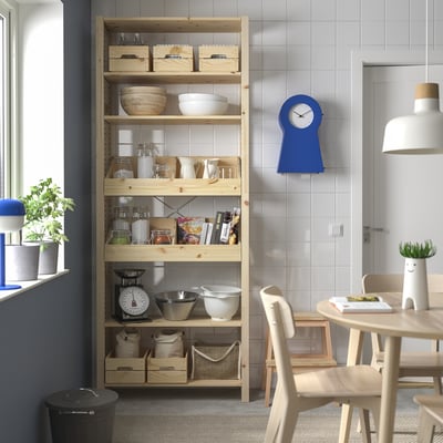 Wooden IVAR shelves with pine finish hold kitchen items, a blue clock, and a white lamp. Space-efficient under a high window.