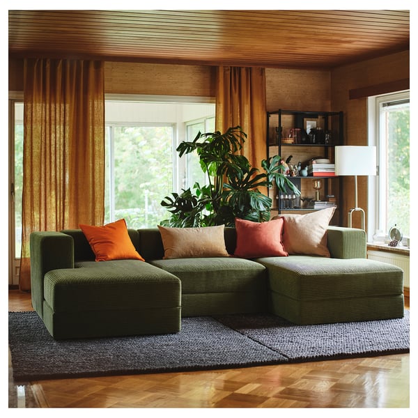 Cosy living room with JÄTTEBO green modular sofa, vibrant pillows, large plant, wooden decor, sunny window.