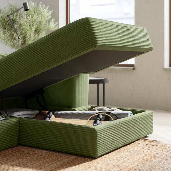 Open green corduroy sofa storage, revealing folded blankets and cushions. Modern design with clean lines.