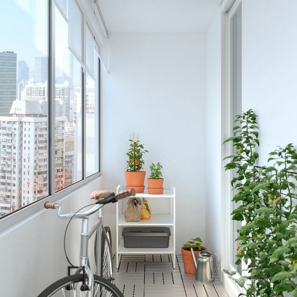 Small balcony with urban view, white JONAXEL shelf holding plants & tools, bicycle, potted greenery.
