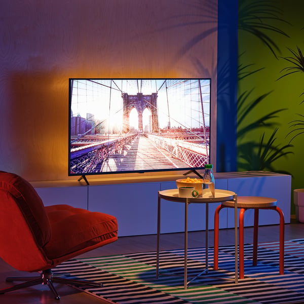 Bright living room with tv showing brooklyn bridge, red chair, snacks, and green plant.