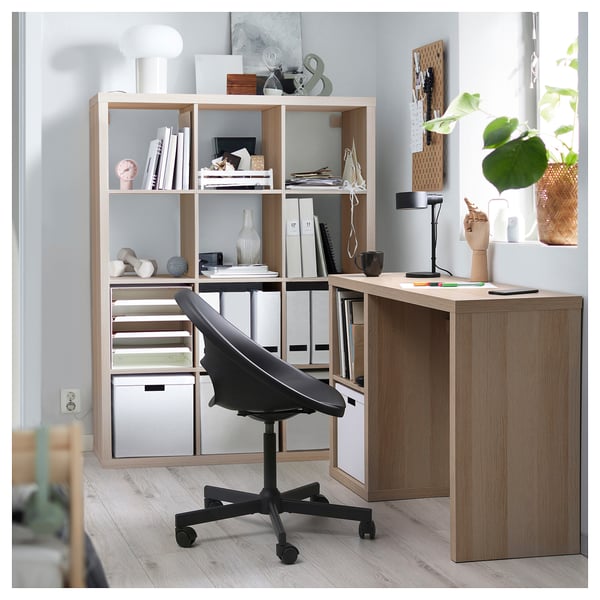 Home office with KALLAX desk, shelves, and black swivel chair. Light wood, organised with books, decor, and storage boxes.