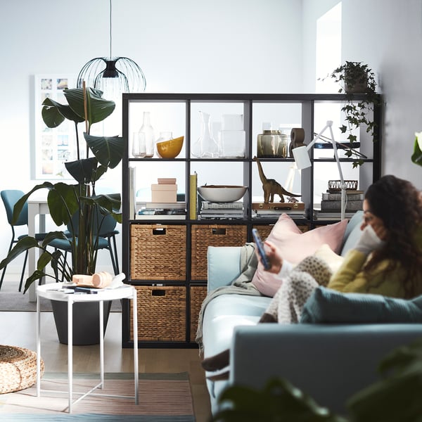 Indoor scene with blue ikea shelf, plants, books, woman on sofa using phone.