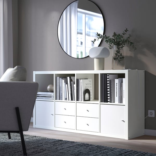 KALLAX storage unit with shelves and drawers, holding books and a vase, against a grey wall in a minimalist living space.