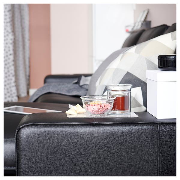 Modern living room with black leather KIVIK sofa, glass bowl, and drink.