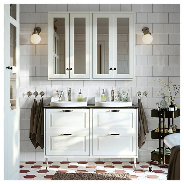 Modern bathroom with white cabinet, black counter, hexagonal flooring, and decorative items, illuminated by spherical lights.