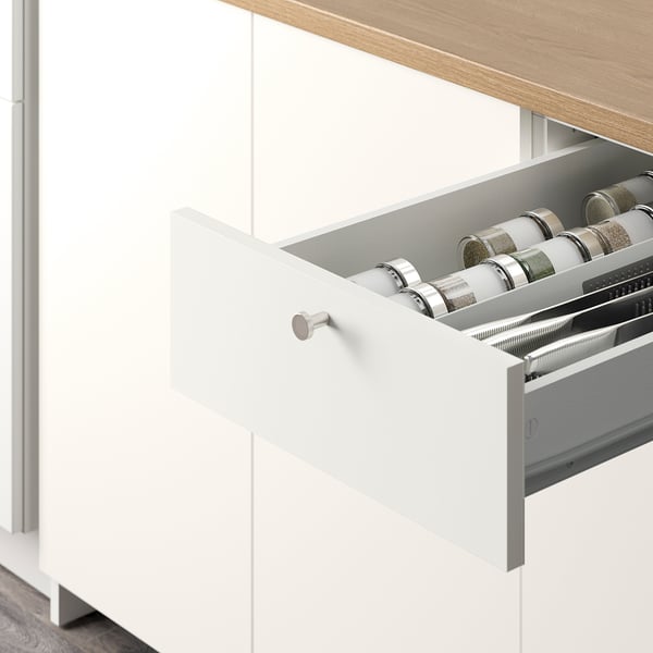 Open white kitchen drawer revealing organised spice rack with glass jars.