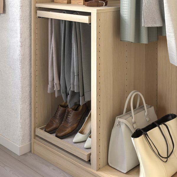 Wooden closet organiser with light-colored shelves, hanging clothes, brown shoes, and beige handbags.