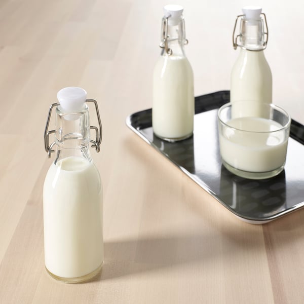 Three glass bottles with white stoppers on a wooden table; one bottle and a cup on a metal tray.