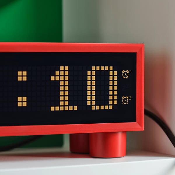 Modern, red digital clock on a white shelf, displaying time 11:11. Shows temperature and humidity, with sleek, pixelated display.