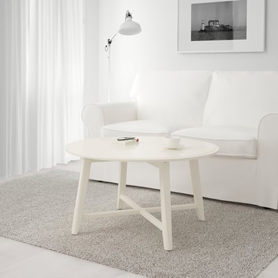 Minimalist living room a KRAGSTA coffee table with modern round design, placed before a white couch, holding a cup and remote on a plush area rug.