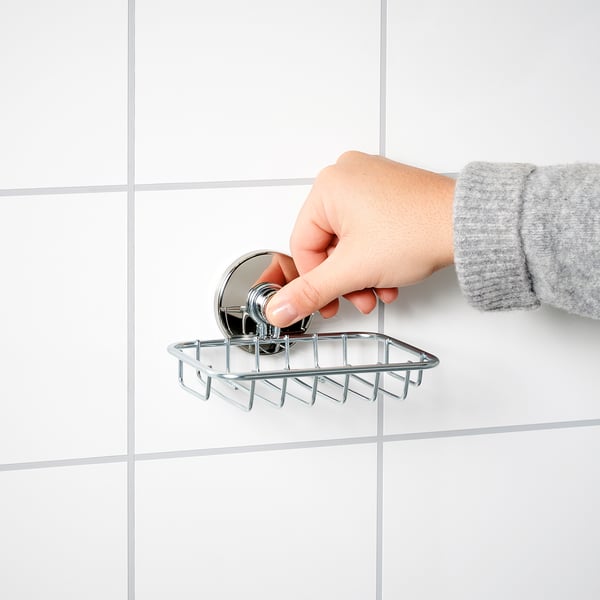 A person adjusts a chrome KROKFJORDEN soap dish suctioned to a white tiled wall.