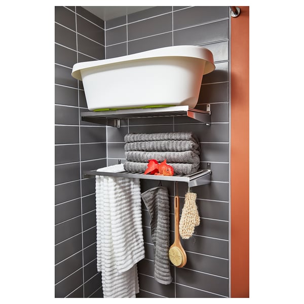 Support shelf in bathroom, holding towels, brushes, tub, grey tiles backdrop.