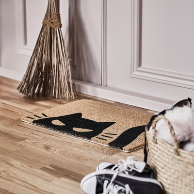 Doormat: KUSTFYR, black cat design, coir fibre, placed near white shoe on wooden floor, smaller than broom.