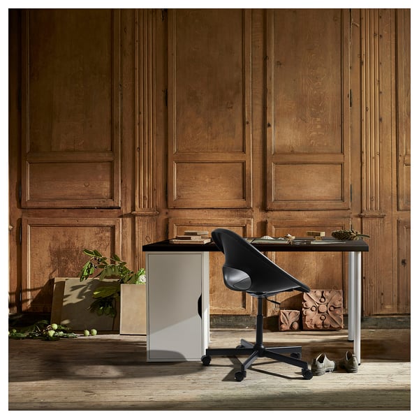 A modern office desk, LAGKAPTEN, with a white top and black chair, set against wooden panels. Minimalist design with practical storage.