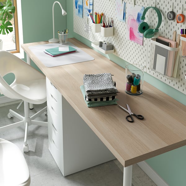 Well-organized home office with a large desk, white chair, and various office supplies, including a tablet, headphones, and a lamp.