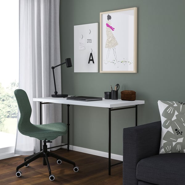 Modern home office with LAGKAPTEN desk, lamp, laptop, basket, art, green chair, sofa, natural light.