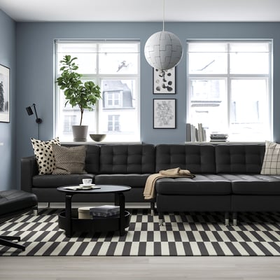 Modern living room with black sofa, striped rug, coffee table, and city views through large windows.