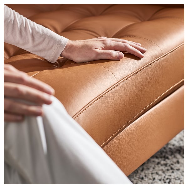 A person sitting on a brown leather LANDSKRONA sofa, gently touching the cushions.