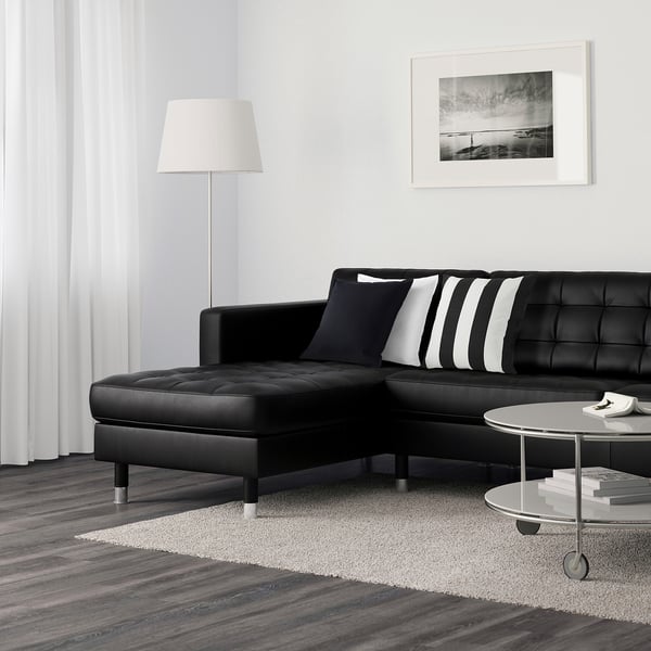 Modern living room with black l-shaped sofa, striped cushions, round coffee table, floor lamp, and wall art.