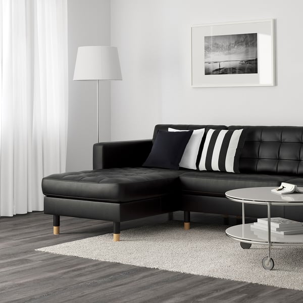 Modern living room with black l-sofa, striped pillows, coffee table, rug, lamp, wall art.
