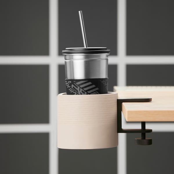 Silver mug with black sleeve in wooden holder on desk. LÅNESPELARE keeps drinks within reach.