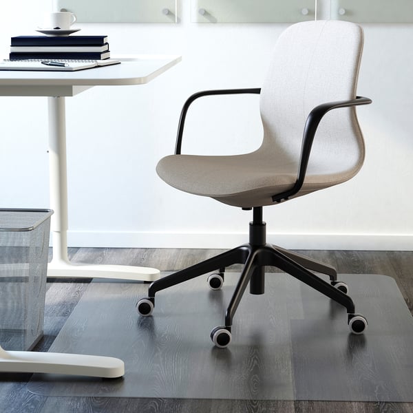 Modern office chair with armrests and wheels on a glass mat, positioned near a white table.