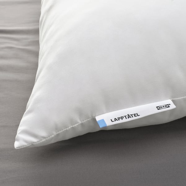 A plush, white pillow on a bed, branded LAPPTÅTEL by IKEA, featuring a soft microfibre finish, promising comfort and support.