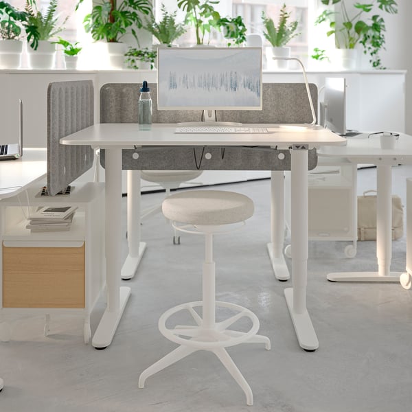 Modern office setup with LIDKULLEN white stool, adjustable desk, and computer monitor, surrounded by greenery.