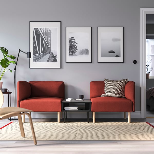 Modern living room with grey walls, red sofas, black table, geometric rug, and art.