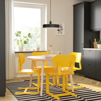 Bright yellow modern dining set with round table and chairs in a cosy kitchen nook, surrounded by dark cabinets and a large window.