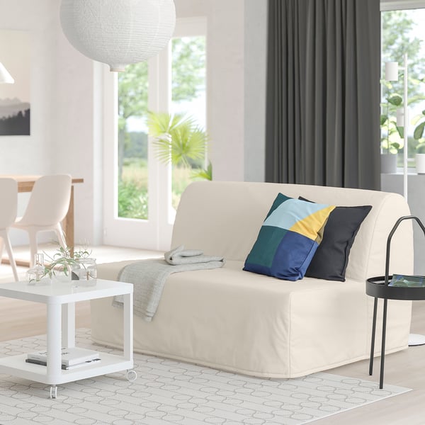 Modern living room with beige sofa-bed, colourful pillows, white coffee table, and a patterned rug.